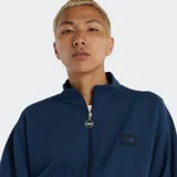 Campera deportiva New Balance de tejido piqué de punto doble, color azul marino, con cierre frontal y cuello alto. Presenta puños y dobladillo con franjas horizontales blancas. Incluye un parche con el logo NB en el pecho y un tirador de insignia NB en el cierre.