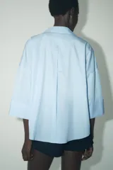 Camisa marrón de popelina con cuello solapa, escote en pico, cierre frontal con botones y mangas anchas con puños.
