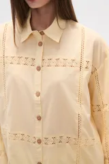 Camisa de algodón blanca, de corte ancho, con botones de madera y detalles de encaje calado en el frente, mangas y ruedo. Tiene cuello camisero y manga larga.