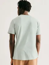 Camiseta blanca de algodón con cuello redondo y mangas cortas. Estampa rectangular con borde negro que contiene la frase "NATURAL ATMOSPHERE" en letras mayúsculas y una imagen de montañas y mar.