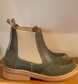 Bota Chelsea color verde oliva, con elásticos laterales en color beige, suela plana de goma color caramelo y tirador trasero.
