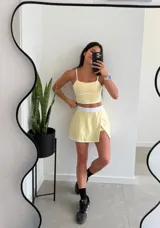 Conjunto deportivo amarillo pálido compuesto por un top con tirantes finos y una minifalda cruzada con short interno.