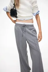 Pantalón gris de sarga con cintura elástica fruncida y cordón ajustable. Piernas amplias con pliegues cosidos, bolsillos laterales discretos y bolsillos decorativos atrás.