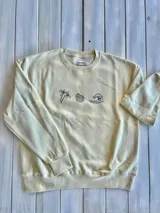 Buzo color crema de corte oversize con cuello redondo y puños y cintura acanalados. Estampado en el frente con motivos playeros: palmera, caracol y ola.