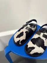 Zuecos con estampado de vaca en blanco y negro, con hebilla ajustable y suela plana.