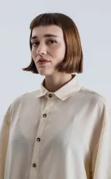 Camisa de manga corta color off-white, con cuello camisero y botones frontales marrones. Corte holgado.