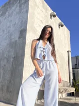 Conjunto celeste a rayas verticales blancas, compuesto por un top halter con lazos y un pantalón palazzo con cintura elastizada.