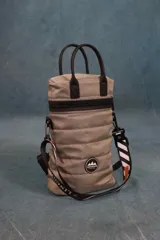 Matera estilo mochila color beige, confeccionada en nylon acolchado y combinada con símil cuero marrón oscuro. Tiene cierre metálico en la tapa, bolsillo interno, asas de mano y correa extensible con diseño de rayas blancas y negras.