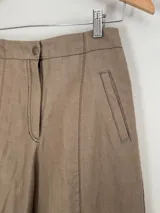 Pantalón de lino y algodón color marrón claro, de tiro medio y piernas anchas. Cuenta con dos bolsillos delanteros y dos traseros con detalles de remaches y atraques.