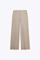 Pantalón de tiro bajo color beige, con bolsillos delanteros y falsos bolsillos de vivo en la espalda. Piernas rectas y cierre frontal con cremallera, botón interior y ganchos.