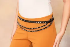 Cinto de cuero negro con textura cocodrilo, adornado con tachas metálicas plateadas. Incluye dos cadenas colgantes entrelazadas con tiras de cuero negro.