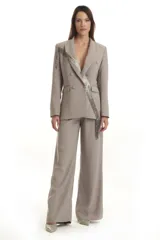 Blazer gris de corte estructurado con doble abotonadura y solapas clásicas. Presenta una aplicación de pedrería en cascada que recorre diagonalmente la prenda.