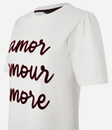 Remera color crema de algodón, corte slim, con cuello redondo y mangas cortas. Estampa frontal con las palabras 'amor', 'amour' y 'amore' en color borgoña.