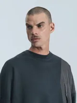 Buzo de cuello redondo, color negro, confeccionado en frisa gamuzada de algodón con recortes en microfibra, creando un efecto de capas. Presenta un bolsillo frontal tipo parche con cierre a presión.