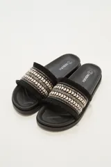Sandalias tipo slide negras con plataforma gruesa. La tira superior es ancha y presenta un diseño étnico con tejido en tonos beige y negro, tachas piramidales y flecos en los bordes.