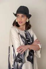 Vestido largo color natural con estampado de hojas de palmera en tonos verdes. Tiene corte amplio tipo túnica, cuello redondo, mangas tres cuartos, bolsillos laterales y ruedo con ribete.