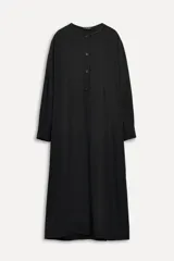Vestido midi negro confeccionado en viscosa. Tiene cuello redondo con detalles deshilachados, manga larga con hombro caído y puños con pliegues. Cuenta con bolsillos laterales ocultos, trabillas y pliegue en la espalda.
