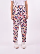 Pantalón babucha de tela estampada con hojas en tonos rosa, naranja y azul, con cintura elastizada y lazo para ajustar.