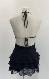 Minivestido negro de encaje con escote halter, abertura en el pecho, espalda descubierta y falda con volados. Incluye short interior.