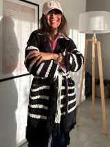 Sacón negro con rayas horizontales blancas, tejido tipo mohair, corte oversize y cinturón ajustable.