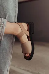 Sandalias bajas color arena, con tiras anchas de cuero y hebilla lateral.