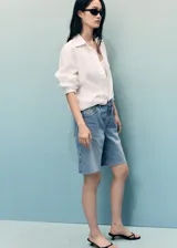 Short de jean azul de tiro medio con cierre de cremallera y botón, cinco bolsillos, diseño recto y bajo deshilachado.