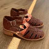 Sandalias franciscanas de cuero color marrón con tiras entretejidas, hebilla lateral y taco bajo de madera.