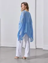 Poncho blanco de tejido calado con lurex, terminación asimétrica y cuello redondo.