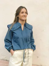 Blusa azul con cuello marinero con volados y lazos en el escote, mangas largas abullonadas con puños elásticos.