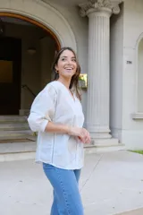 Blusa blanca de manga larga con elástico en puños, escote en pico y cierre frontal con botones. Detalles de bordados con hilado en tonalidad camel y acabado con entredoses a tono.