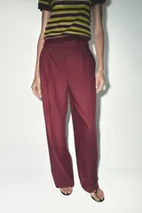 Pantalón de vestir color borgoña, de tiro alto y pierna ancha, con bolsillos laterales y cierre frontal con cremallera y ganchos metálicos.