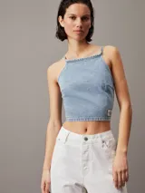 Top corto de denim rígido de algodón celeste, con cuello alto, espalda abierta con cierre anudado y logo de Calvin Klein en el bajo.