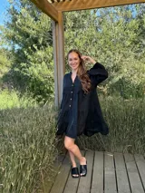 Vestido corto negro de lino, con escote en V, botones frontales y mangas largas acampanadas con volados.