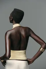 Top color crema con cuello halter, espalda descubierta, detalle de frunces y pieza metálica en forma de sol en el delantero.