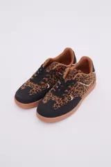 Zapatillas bajas de cuero sintético con estampado animal print, puntera y cordones negros, suela color caramelo y detalle en el talón color blanco.