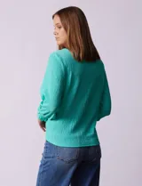 Blusa verde agua de tejido texturado marca Ruby Rd, con cuello a la base, escote en V con aplique metálico, mangas tres cuartos con puños elásticos y terminación de ruedo con nudo.