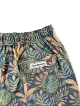 Short de baño blanco con estampado de hojas de palmera en tonos verde, rojo y amarillo.