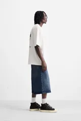 Camiseta blanca de corte relajado, cuello redondo y manga corta. Presenta un estampado de gráficos y textos combinados a contraste en la parte delantera y trasera.