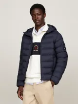 Campera Tommy Hilfiger acolchada color azul marino, con capucha fija ajustable con cordón, cierre de cremallera frontal, dos bolsillos laterales y parche engomado con el logo de la marca en la manga.