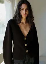 Chaqueta negra de punto con cuello pico, cierre frontal con botones dorados con efecto joya y mangas largas.