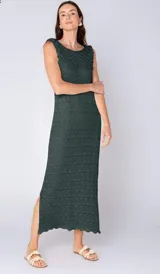 Vestido largo sin mangas de tejido calado, color verde oscuro, con cuello redondo y aberturas laterales. Presenta un patrón de punto texturizado a lo largo de todo el cuerpo y terminaciones onduladas en el ruedo.