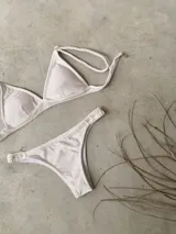 Conjunto de bikini blanco con textura, compuesto por un corpiño de triángulo fijo con breteles regulables y almohadillas desmontables, y una bombacha vedetina con frunce elástico en los costados.