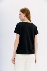 Remera negra de algodón con cuello redondo y mangas cortas. Presenta un bordado de flores con canutillos y piedras en el hombro izquierdo.