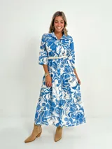 Vestido largo camisero con estampado floral en tonos rosados y blancos, con cuello camisero, manga 3/4 y falda escalonada. Incluye cinturón fino de soga.