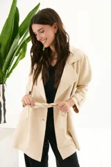 Trench simil gamuza color beige, con cuello de solapa muesca, cuatro botones delanteros, bolsillos laterales y cinturón a la altura de la cintura.