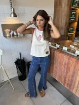 Pantalón de jean azul oscuro, tiro alto, con pierna flare y abertura frontal en el ruedo. Presenta costuras verticales marcadas en el frente de ambas piernas.