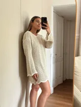 Vestido corto tejido en algodón y lurex color crudo, con punto pavo real, manga larga y escote en la espalda.