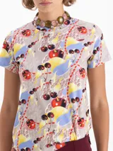 Remera de algodón pima con estampado de cerezas y otros motivos abstractos en colores rojo, amarillo, azul y gris. Presenta escote redondo, mangas cortas y una pequeña boca bordada en el delantero.