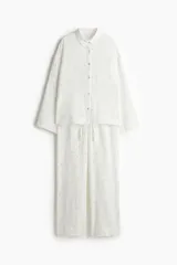Conjunto de pijama de dos piezas en muselina de algodón suave color blanco con estampado floral. Incluye camisa de manga larga con cuello, botones y bolsillo superior, y pantalón recto con cintura elástica y cordón ajustable.