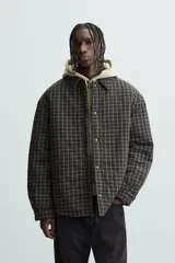 Sobrecamisa de hombre con corte relaxed fit, confeccionada en tejido de algodón acolchado con estampado a cuadros en tonos marrón, negro y beige. Tiene cuello solapa, manga larga con puños abotonados, bolsillo tipo parche en el pecho, aberturas laterales en el bajo y cierre frontal con botones a presión.